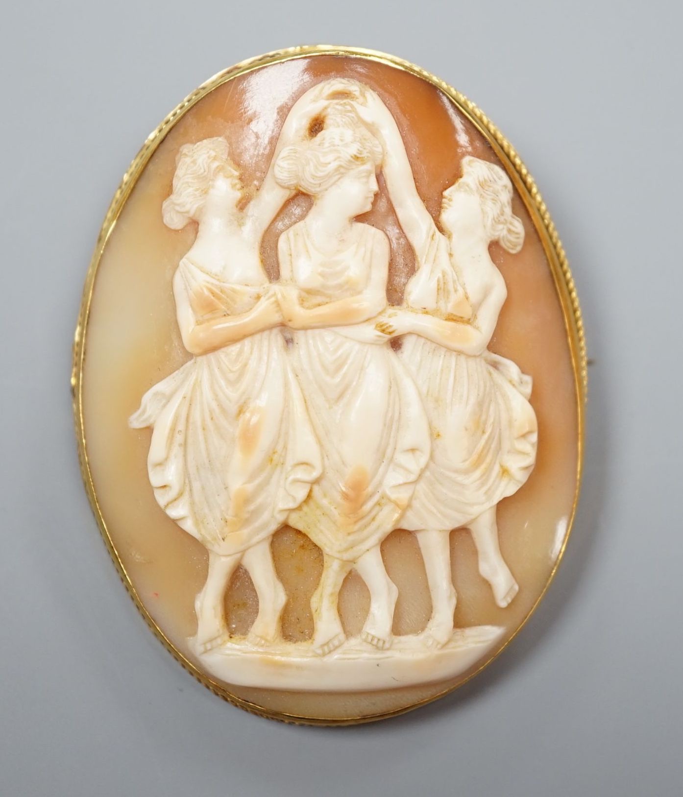 A yellow metal mounted oval cameo shell pendant brooch, carved with The Three Graces, 62mm, gross weight 21.4 grams.